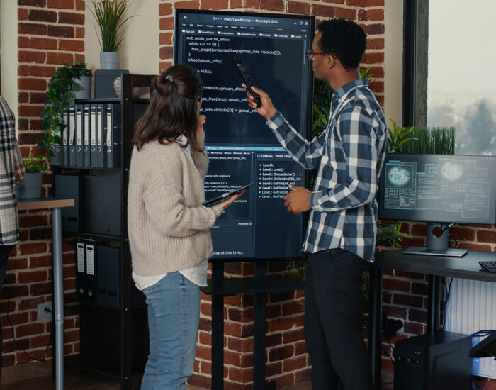 Team of database admins analyzing source code on wall screen tv comparing errors using digital tablet