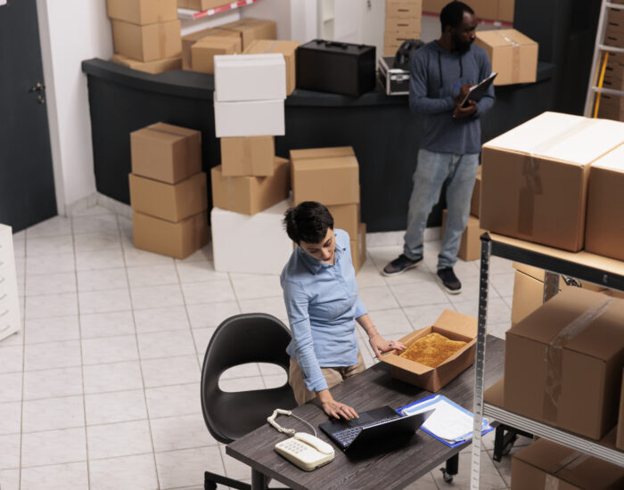 Top view of warehouse supervisor packing client clothes order in cardboard box while checking shipping details